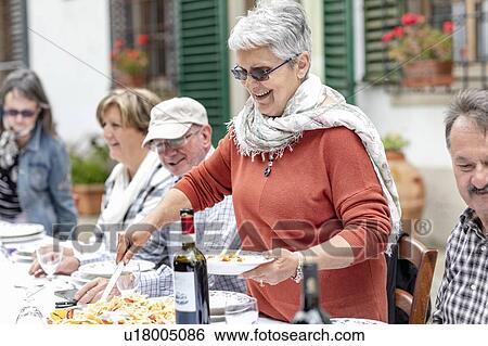 Stock Photograph - Woman serving pasta at family lunch in garden, Florence, Italy. Fotosearch