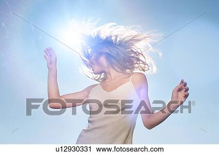 Stock Image - Woman swishing her hair outside infront of lensflare. Fotosearch
