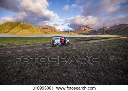 Stock Image - Woman traveller enjoying scenic view beside vehicle, Landmannalaugar, Highlands, Iceland. Fotosearch