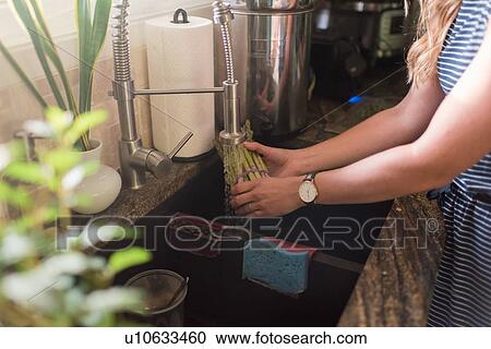 Stock Image - Woman washing artichokes under kitchen tap. Fotosearch