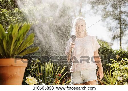 Woman watering plants with water hose in garden View Large Photo Image Stock Image - Woman watering plants with water hose in garden. Fotosearch