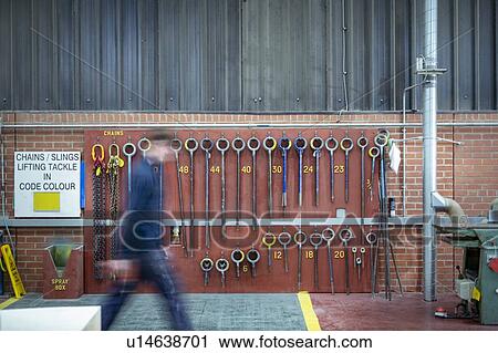 Stock Image - Worker walking passed lifting hooks in steelworks. Fotosearch