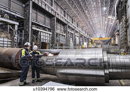 Stock Photograph - Workers inspecting large steel roller in forge of steelworks. Fotosearch