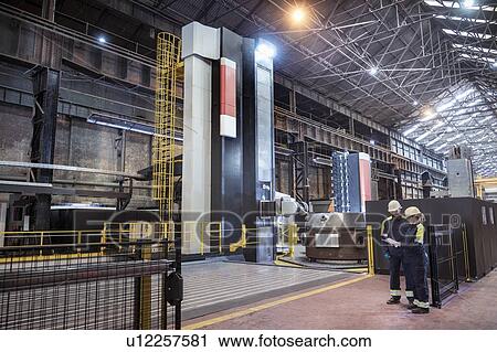 Stock Image - Workers with specialist large 3D cutting CNC lathe in steelworks. Fotosearch