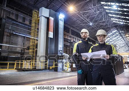 Stock Image - Workers with specialist large 3D cutting CNC lathe in steelworks. Fotosearch