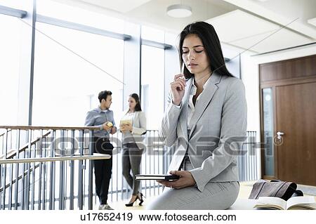 Stock Photo - Young businesswoman in office, colleagues talking in background. Fotosearch