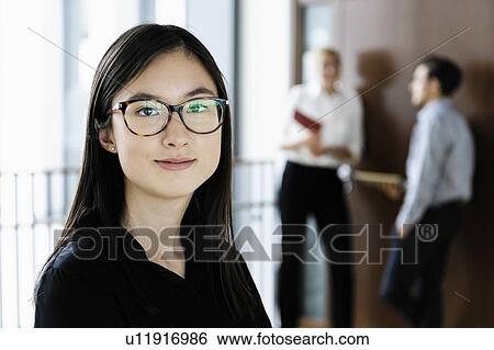 Young businesswoman in office, colleagues talking in background View Large Photo Image Stock Photograph - Young businesswoman in office, colleagues talking in background. Fotosearch