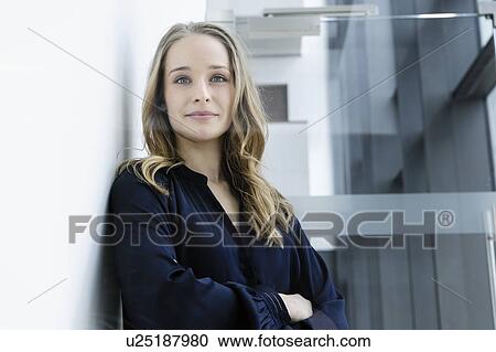 Stock Image - Young businesswoman leaning against white wall in office building. Fotosearch
