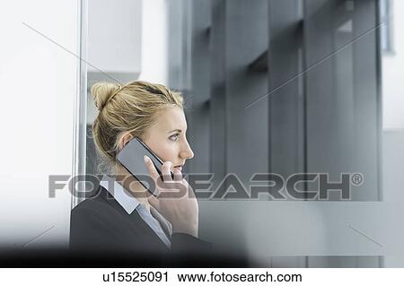 Stock Image - Young businesswoman talking on smartphone at corridor of office building. Fotosearch