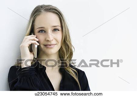 Stock Photography - Young businesswoman talking on smartphone against white wall. Fotosearch