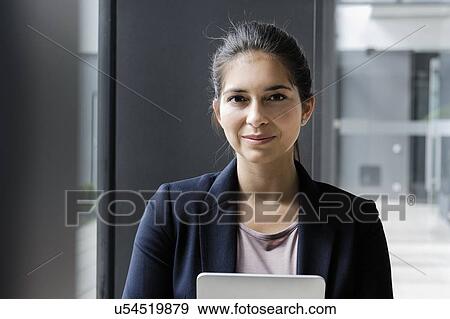 Stock Photo - Young businesswoman using digital tablet at corridor of office building. Fotosearch