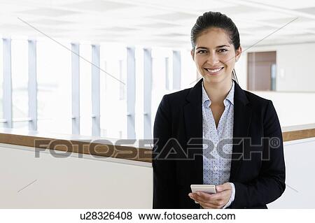 Young businesswoman using smartphone at corridor of office building View Large Photo Image Stock Photo - Young businesswoman using smartphone at corridor of office building. Fotosearch
