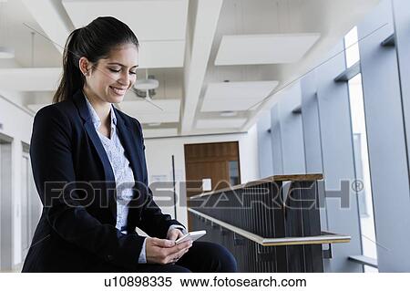 Stock Photography - Young businesswoman using smartphone at corridor of office building. Fotosearch