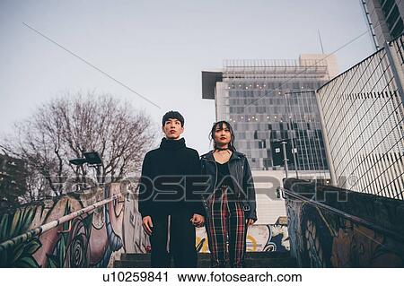 Stock Image - Young couple holding hands at top of concrete stairs, Milan, Italy. Fotosearch