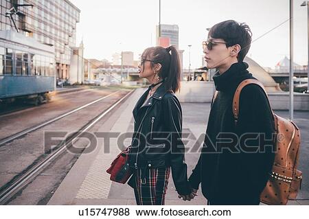 Stock Photo - Young couple holding hands waiting by tram tracks, Milan, Italy. Fotosearch