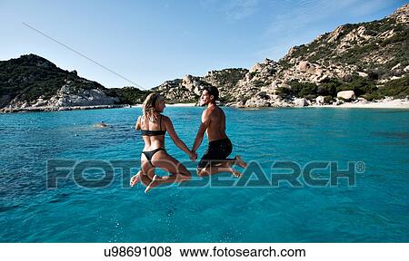 Stock Photo - Young couple jumping into sea from yacht, La Maddalena island, Sardegna, Italy. Fotosearch