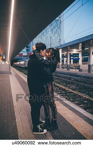 Stock Image - Young couple kissing on train station platform, Milan, Italy. Fotosearch