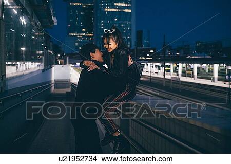 Picture - Young couple laughing and hugging in train station, Milan, Italy. Fotosearch