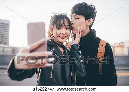 Stock Photo - Young couple taking selfie on street, Milan, Italy. Fotosearch