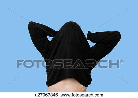 Stock Photograph - Young man having trouble putting on sweater. Fotosearch