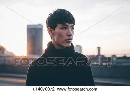 Stock Image - Young man, high-rise building in background, Milan, Italy. Fotosearch