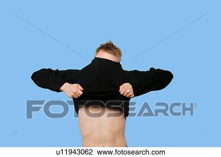 Stock Image - Young man struggling to pull down t-shirt over blue background. Fotosearch