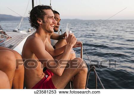 Stock Image - Young men enjoying champagne on sailboat, Italy. Fotosearch