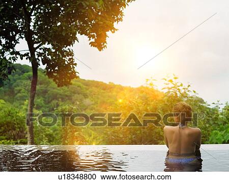 Stock Image - Young Woman in Swimming Pool at sunset. Fotosearch