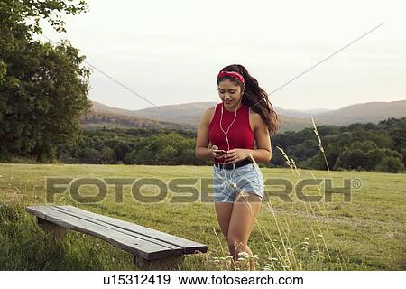 Stock Photo - Young woman listening to music with earphones, hills in background, Wilhelminenberg, Vienna, Austria. Fotosearch