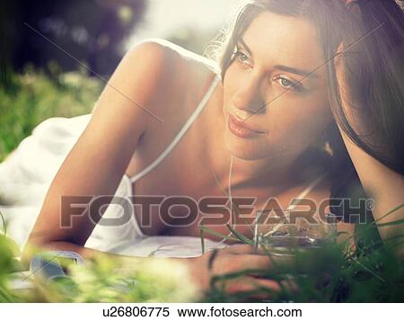 Young woman lying in meadow, leaning on elbow, with drinking glass View Large Photo Image Stock Photography - Young woman lying in meadow, leaning on elbow, with drinking glass. Fotosearch
