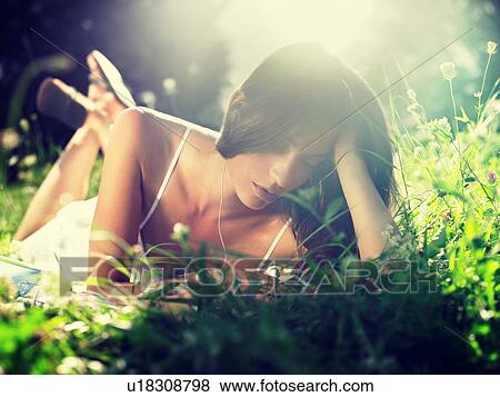 Stock Photo - Young woman lying in meadow listening to mp3 player. Fotosearch