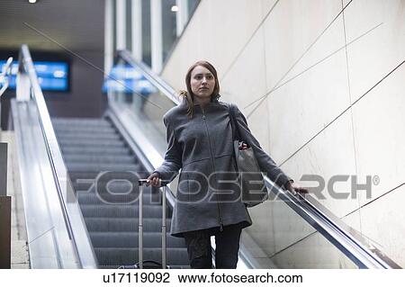 Stock Image - Young woman on escalator in train terminal. Fotosearch