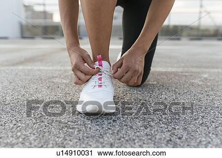 Stock Image - Young woman tying shoelace on rooftop deck. Fotosearch