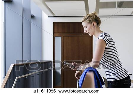 Stock Photograph - Young woman using smartphone at corridor of office building. Fotosearch