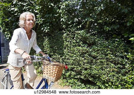 Stock Photo - Active senior woman riding bicycle in backyard. Fotosearch