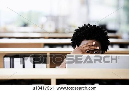 Stock Image - African American Man using computer in office with stress. Fotosearch