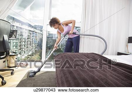 Stock Image - African American woman vacuuming in bedroom. Fotosearch