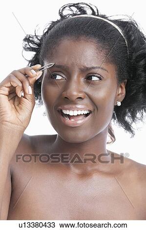 Stock Image - African American young woman tweezing her eyebrows over white background. Fotosearch