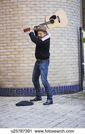 Aggressive young man breaking guitar against brick wall on street View Large Photo Image Stock Image - Aggressive young man breaking guitar against brick wall on street. Fotosearch