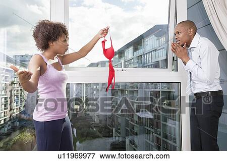 Angry young woman holding bra in front of guilty man at home View Large Photo Image Stock Photo - Angry young woman holding bra in front of guilty man at home. Fotosearch