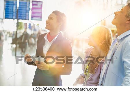 Stock Image - Attractive airport staff holding boarding pass while looking at the monitor in airport. Fotosearch
