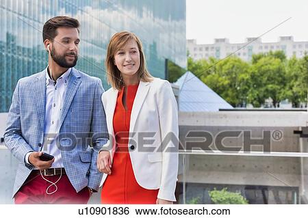 Stock Photograph - Attractive businessman and businesswoman standing outside office building. Fotosearch