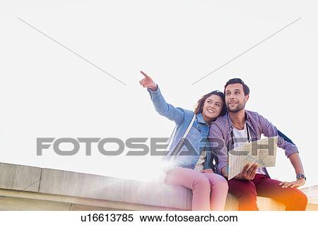 Stock Photography - Attractive man holding map while sitting and talking to his girlfriend. Fotosearch