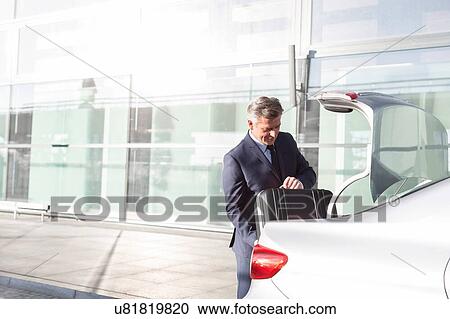 Attractive mature businessman putting his luggage on car trunk View Large Photo Image Stock Image - Attractive mature businessman putting his luggage on car trunk . Fotosearch