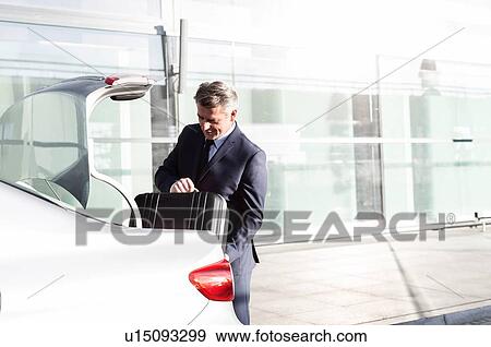 Attractive mature businessman putting his luggage on car trunk View Large Photo Image Stock Photo - Attractive mature businessman putting his luggage on car trunk . Fotosearch