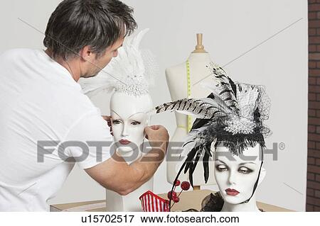 Stock Photo - Back view of male fashion designer adjusting feather fascinator on mannequin. Fotosearch