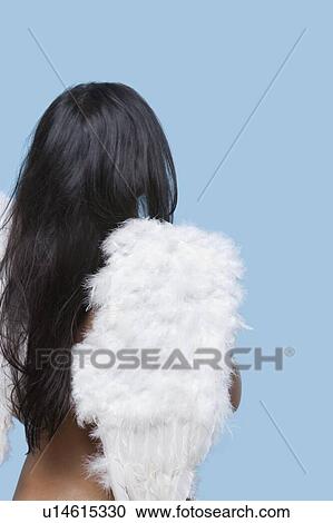 Stock Image - Back view of young woman wearing artificial wings over blue background. Fotosearch