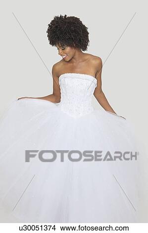 Picture - Beautiful African American bride in white wedding dress standing against plain background. Fotosearch