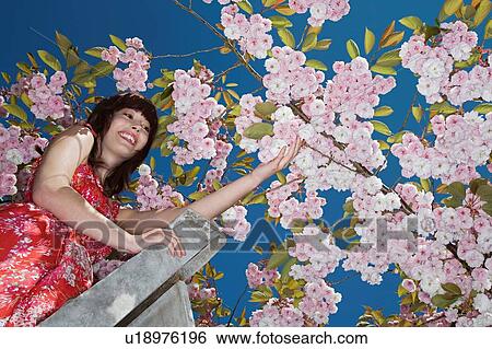Stock Photograph - Beautiful redhead woman wearing dress by cherry blossom. Fotosearch