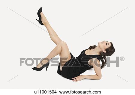 Beautiful young woman in dress sitting on floor with feet up against white background View Large Photo Image Picture - Beautiful young woman in dress sitting on floor with feet up against white background. Fotosearch